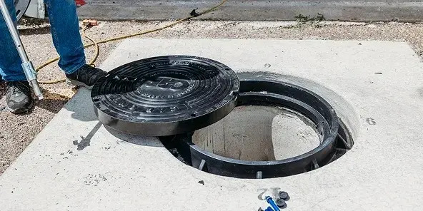 Workers repairing a manhole cover in San Diego, with tools and equipment visible on the street.