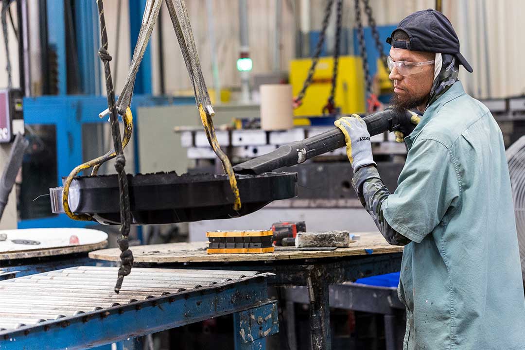 Un operario utiliza maquinaria en una fábrica para crear una placa metálica, destacando la producción de tapas de registro.