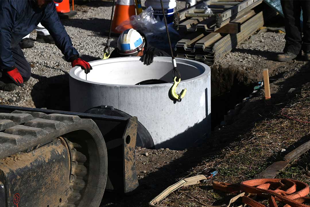 A man in safety gear inspects and works on a large concrete tank for man hole cover at a construction site.