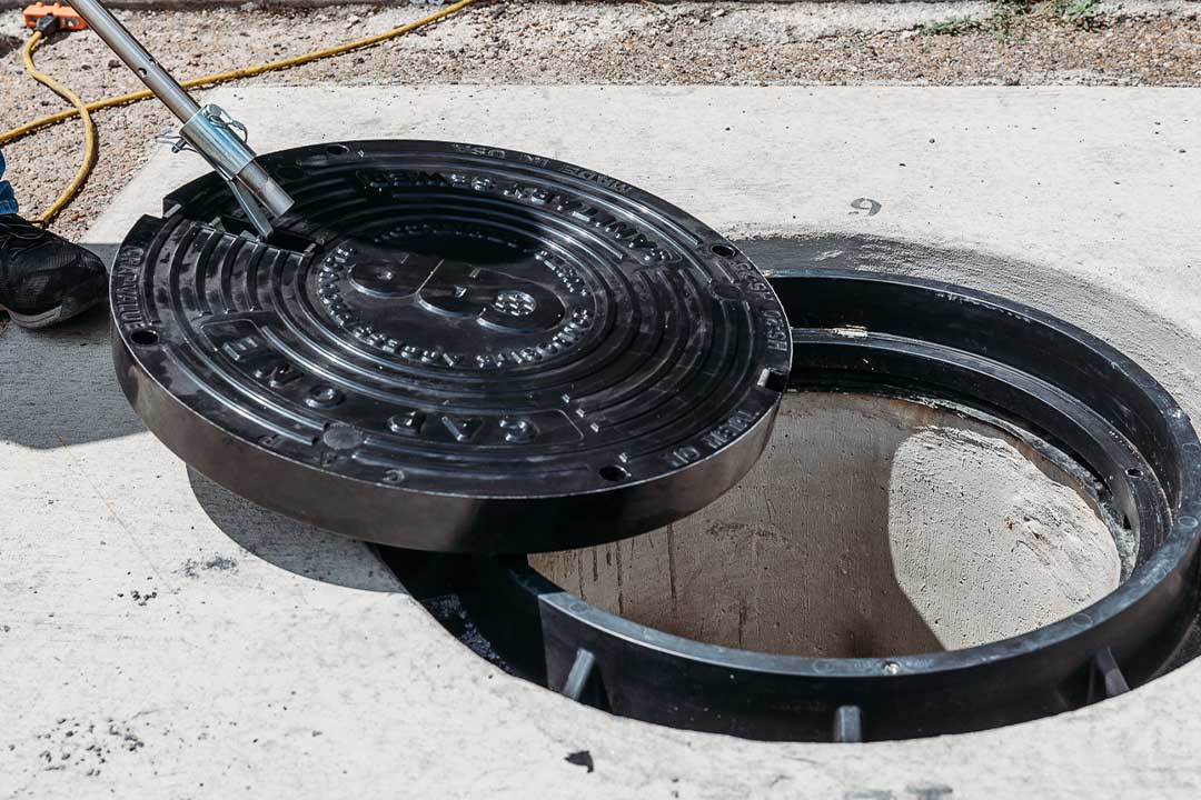 CAP manhole cover. man operates a hose to wash out a manhole, ensuring it is clear of blockages and contaminants.